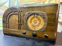 Front view of vintage General Electric radio showing wood casing, fabric speaker grille, analog dial and three knobs.