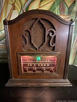 Front view of vintage Sparton tube radio in wooden cabinet with ornate carved front panel and fabric speaker grille.