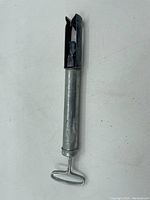 Photo of the full tool showing the black bottle or cap opener end, cylindrical metal body, and the T-shaped handle.