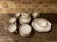 Overall view of cups, saucers, plates, creamer, and sugar dish arranged on counter showing floral and gold lattice pattern on white porcelain.