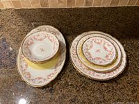 Photo of the bowls stacked on the oval platter, along with assorted plates showing pink floral Bridal Rose pattern with gold trim.