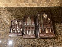 Three boxed sets displayed: coffee spoons, dessert set with forks and server, and a 4-piece dinner set.