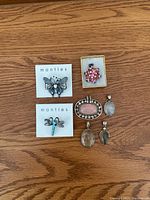 Top-down photo of the 2 brooches and 5 pendants arranged on a wooden surface, showing the full lot content and details.