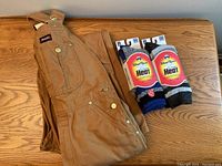 Dickies brown canvas overalls folded, paired with two new pairs of Wind River warm socks on wood surface