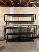 Front view of black metal shelving unit with five shelves attached against wall in basement
