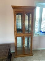 Full view of oak curio cabinet against wall with glass doors and ornate molding.