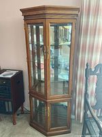 Full view of the oak curio cabinet showing its height, octagonal shape, glass shelves, and brass hardware.