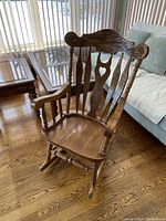 Full view of the oak rocking chair showing its carved wooden backrest, curved armrests, and rockers on the floor.