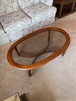 View of oak oval coffee table showing glass center, wooden frame, and turned legs.