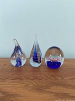 Front view of three glass paperweights on wooden surface showing shapes and internal color designs