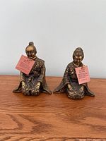 Pair of seated brass samurai statues with red informational tags, showing male and female figures dressed in traditional engraved attire.