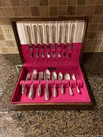 Full set of silverplated silverware including knives on the top row and forks, spoons on the bottom row, displayed inside a wooden box with red felt lining.