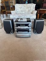 Front view of the TEAC DC-D2831 digital compact hi-fi system stacked with two speakers on either side, showing the entire setup on carpet in a living room environment.