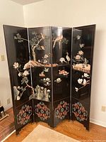 Four-panel black lacquer folding screen with bird and floral painted scenes in a residential room corner.
