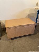 Front and side view of rectangular vintage cedar lined chest with tan vinyl padded top and matching vinyl exterior, standing on four short wooden legs