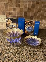 Two vintage flower-shaped glass dishes, one footed and larger, one smaller and flat, on granite counter with original Walter-Glas boxes behind them.