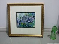 Framed watercolor painting with gold ornate frame and cream mat, showing rustic fence and foliage scene.