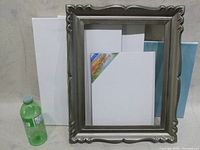 Three canvases including one blue background canvas, one painted canvas, one plain white canvas, and an empty decorative frame displayed with a water bottle for scale.