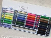 Full view of the 64-piece thread and bobbin set inside a transparent plastic carrying case, showing all spools and bobbins arranged by color.