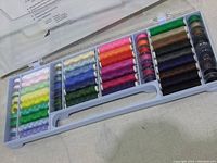 Clear view of 64 pieces sewing threads and bobbins in a plastic carry case with organized color arrangement.