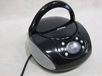 Front and top angle of black Sylvania portable CD player showing control buttons, digital display, speaker grills, and handle.