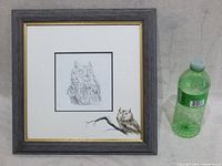 Front view of the framed owl drawing with a small green bottle for size reference.