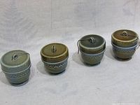 Four vintage ceramic egg coddlers with lids on, showing their exterior glazed finish in green to brown tones and decorative band pattern.