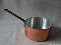 Top side view of small copper pot showing interior lining, round shape, and long metal handle.