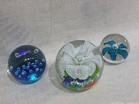 Front view showing the three glass paperweights arranged by size on a light fabric background.