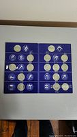Full view of blue folder open showing two pages of silver-tone coins paired with white sport icons, 10 coins per page arranged in rows.