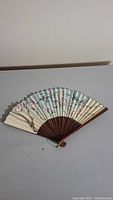 Antique hand fan folded, showing the painted floral fabric and wooden ribs.