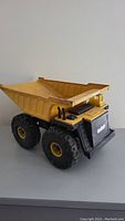 Front angled view of the antique yellow and black toy dump truck showing large rubber tires and the tilting bed.