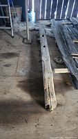 Full length view of the single barn beam laid on plywood floor showing the beam's worn surface, wood grain, and cutouts.