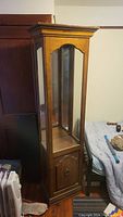 Full view of the tall wooden display cabinet showing glass panels on three sides and the bottom storage cabinet door.
