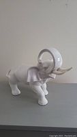 White ceramic elephant figurine with trunk raised shown side angle, highlighting details and glossy finish
