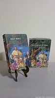 Holy Bible King James Version and The Rainbow Bible standing with covers facing forward, both showing illustrated cover art of Jesus with children under a tree.