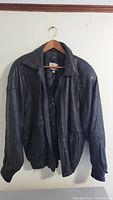 Full view of the black lambskin leather jacket hung on a hanger, showing front and shape.
