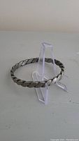 Side view of circular twisted metal bracelet displayed on a clear plastic stand.
