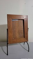 Front view of wooden picture frame with metal stand showing wood grain and frame opening.