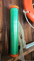 Green plastic wrap roll with orange end caps placed on wooden surface.