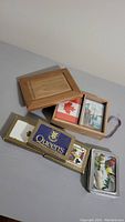 Overview showing wooden box with sliding lid and multiple decks of playing cards including Queens brand and metal tin case with bird image.