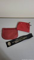 Photo of two red purses and a black Johns Hopkins University Alumni Association bookmark, showing details of the purses and text on the bookmark.