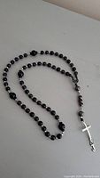 Full rosary beads laid out showing black and purple beads with silver accent beads and silver cross pendant.