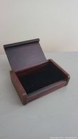 Open view of small wooden display box showing black padded interior.