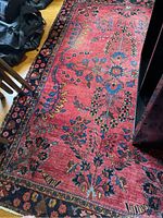 Overhead view showing red floral pattern with navy border, partially under furniture and black bags