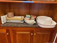 Wide shot of the entire baking dish and serving bowl collection displayed on a kitchen counter, including rectangular bakeware, platters, and colorful smaller bowls.