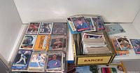 Photo showing assorted baseball cards displayed in plastic sleeves and a box of cards next to them.