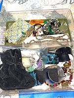 Top view showing handwoven bracelets, chains, and other costume jewelry in a plastic container.