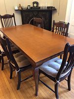 Photo showing full view of wood dining table with six chairs around it. Medium brown finish. Chairs have front and side views visible.