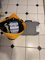 Top-down view of yellow bag with rope and splicing handbook inside, gray plastic Dremel case beside it